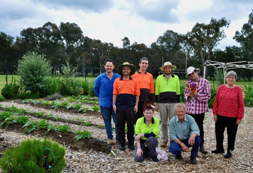 A group of adults in gardening clothes pose next to garden beds