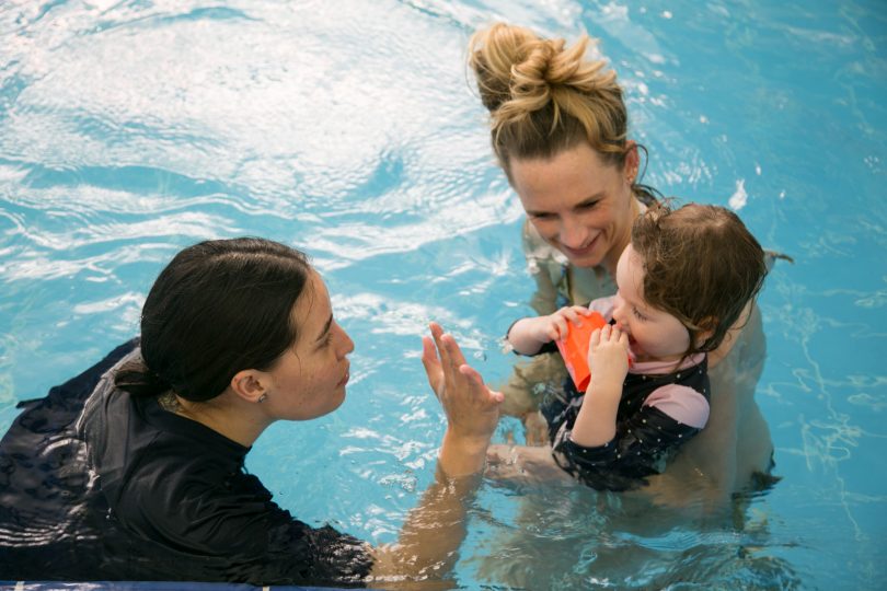 Mother, toddler and instructor in pool at swim school