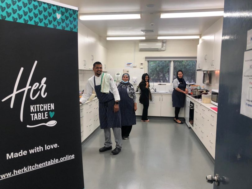 Group smiling in kitchen with her kitchen table banner in foreground