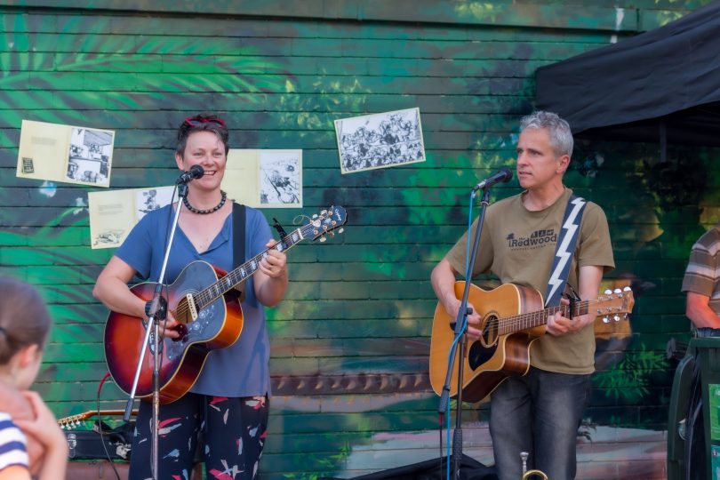 Two people play guitar in front of mural