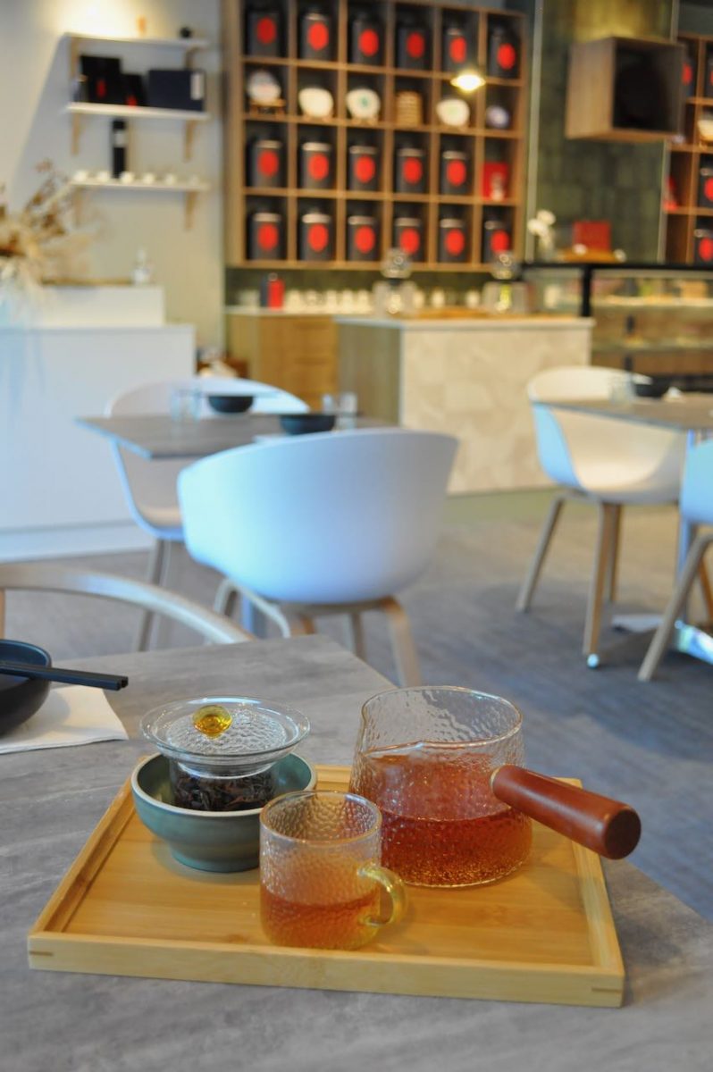 Glass teapot and cup against backdrop of tea shop