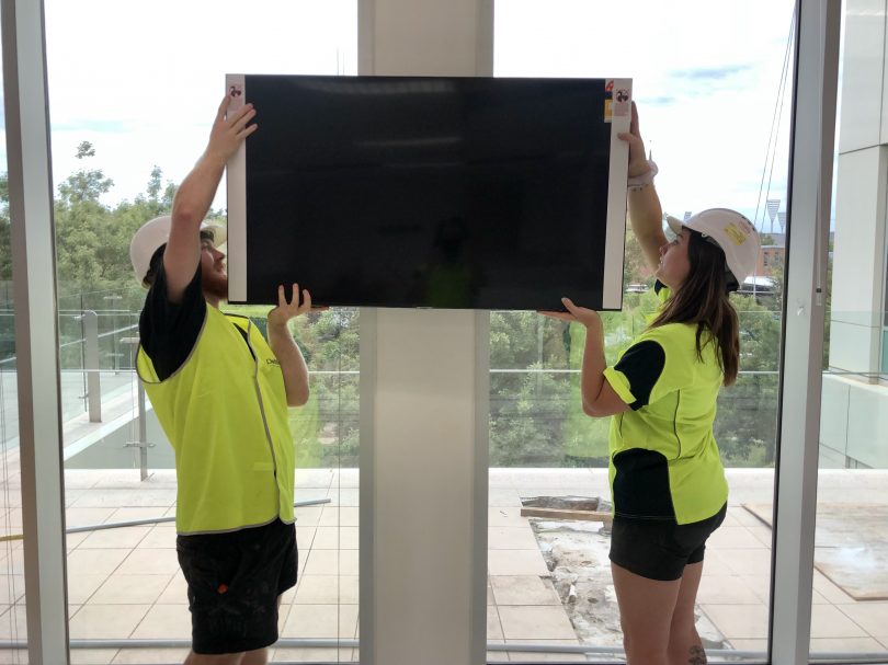 Man and woman tradies erecting TV on wall