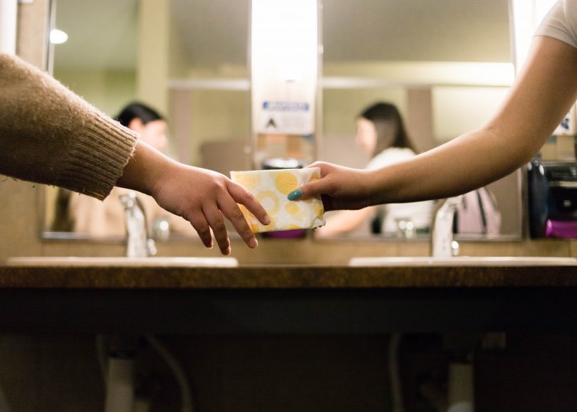 girl handing her friend a pad in the bathroom