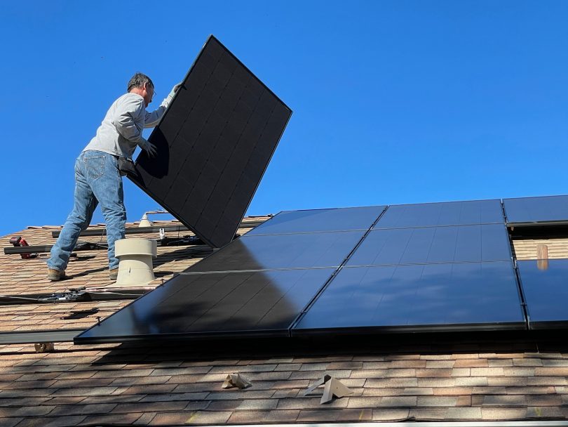 A worker is installing solar panel on the roof of a house