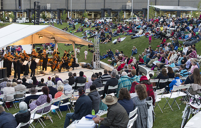 Crowds sit in chairs and on the lawns at Queanbeyan River as the Canberra Symphony Orchestra plays for music by the river