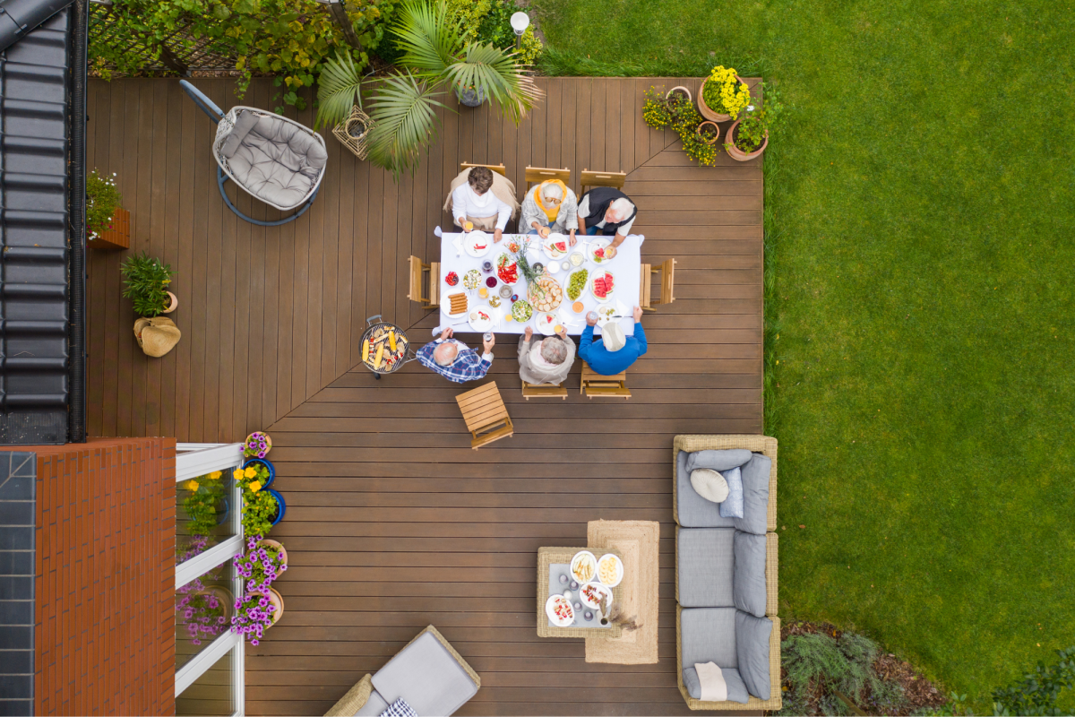 a group of people sitting around a dining table on a deck outside eating a meal