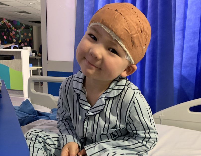 A boy on a hospital bed with his head wrapped in bandages