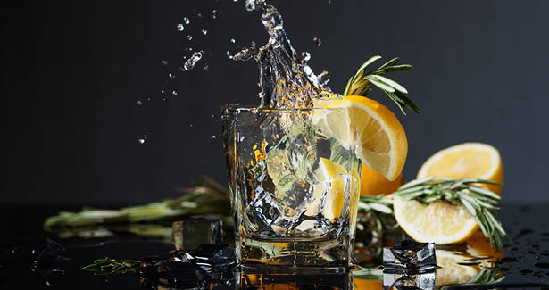 ice splashing into glass with lemons behind it