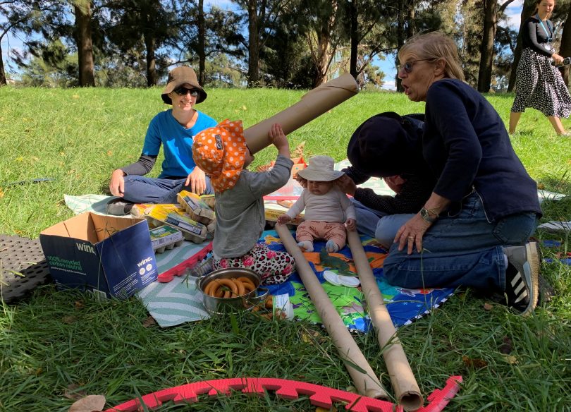 People sitting on a rug on the grass and playing with objects