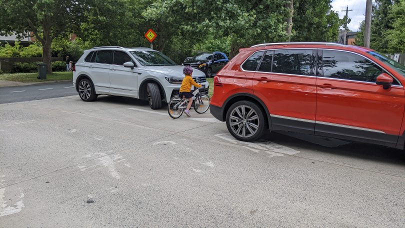 child on bike crossing road between cars