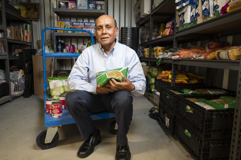 Man sitting on dolly holding pasta and surrounded by tinned food