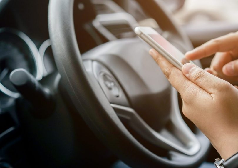 Hand using smart phone in a car near a steering wheel