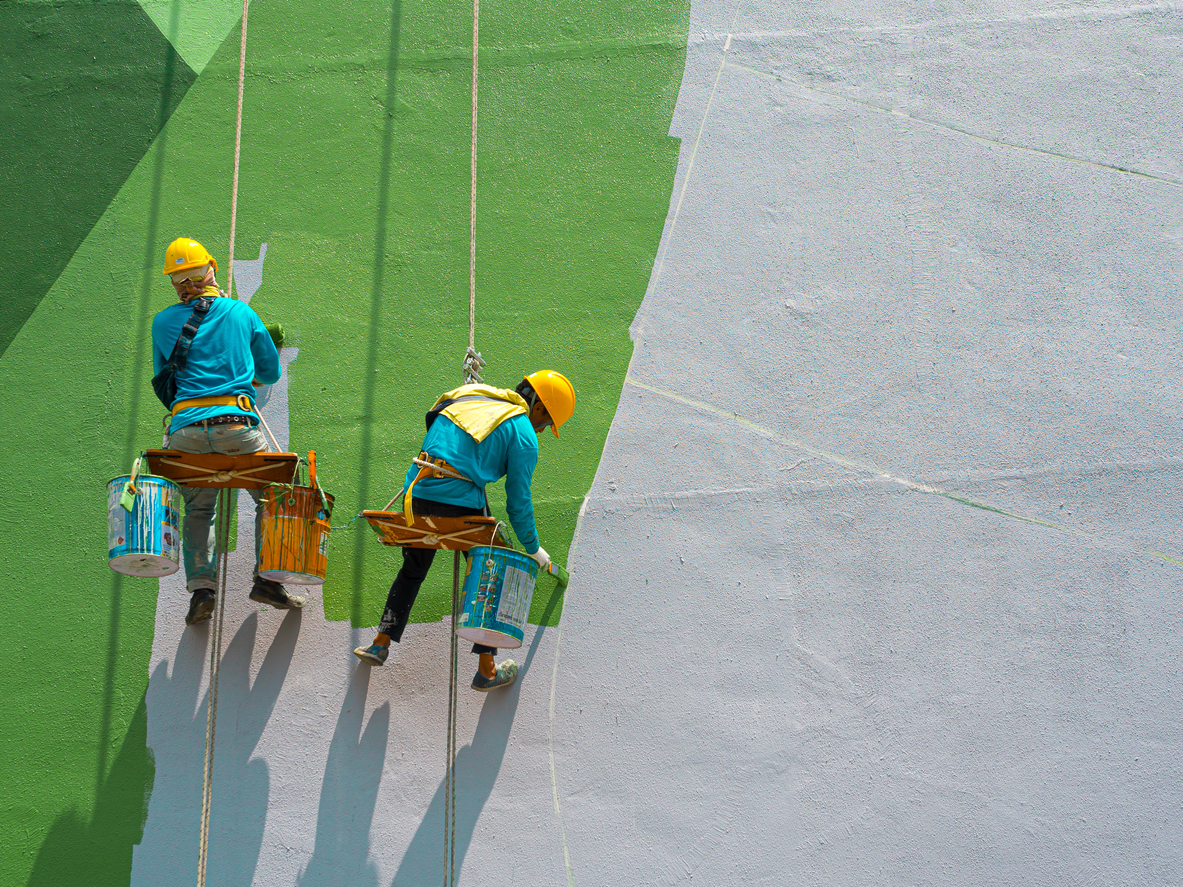 Two painters are painting the exterior of the building on a dangerous looking scaffolding hanging from a tall building.