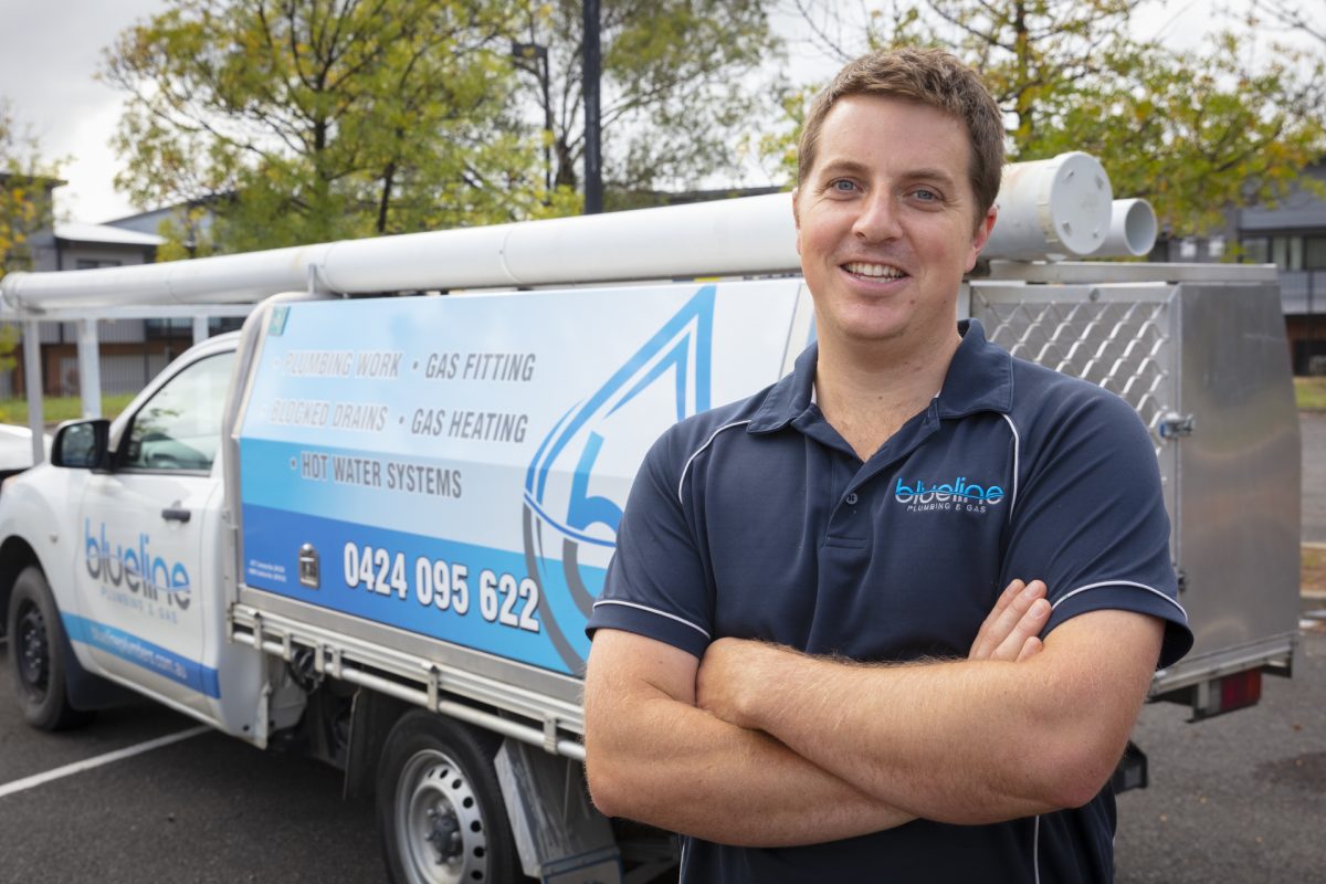 a man with crossed arms wearing uniform standing in front of a branded work truck