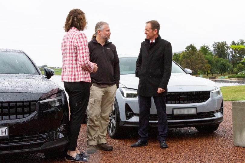 Three people standing in front of electric vehicles