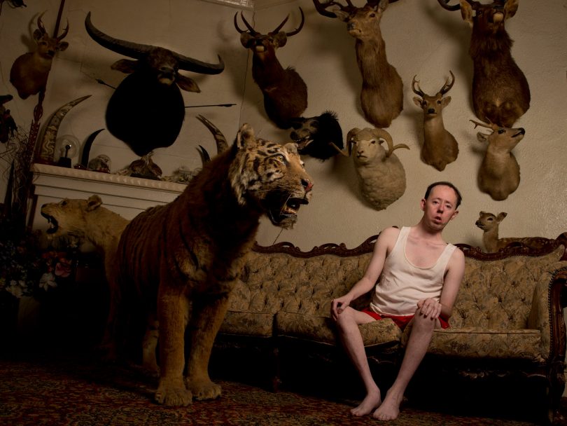 Man sitting on couch surrounded by taxidermy animals