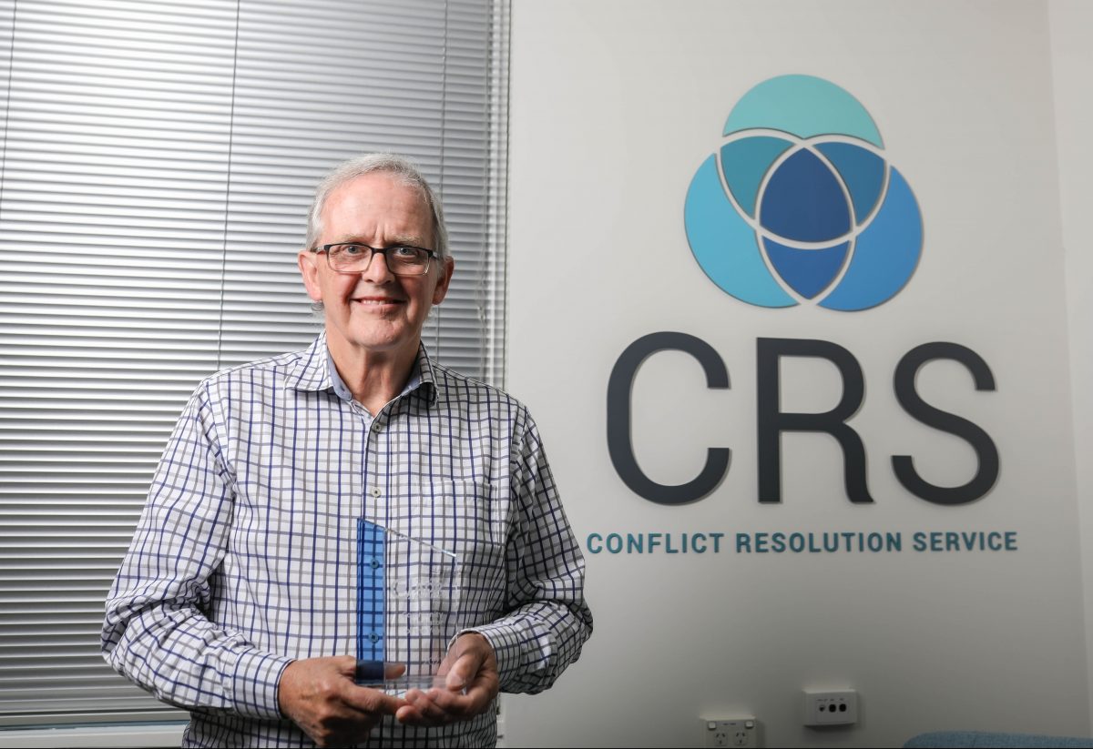 Mediator Nigel Biginel holds an award in front of the Conflict Resolution Service logo