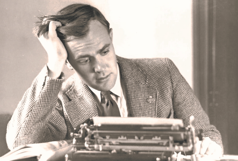 a black and white photo of a person sitting at a typewriter resting their head in one hand