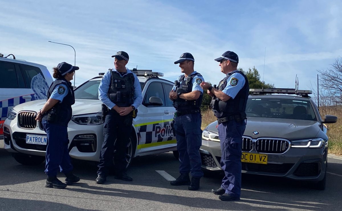 Police officers gathered on a road in front of cars