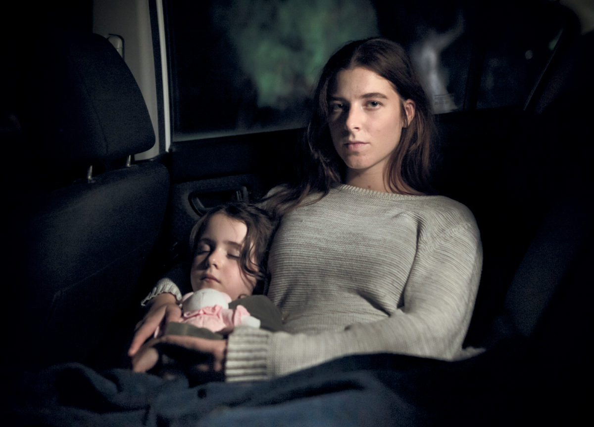 A child sleeps beside her mother in the back seat of a car.