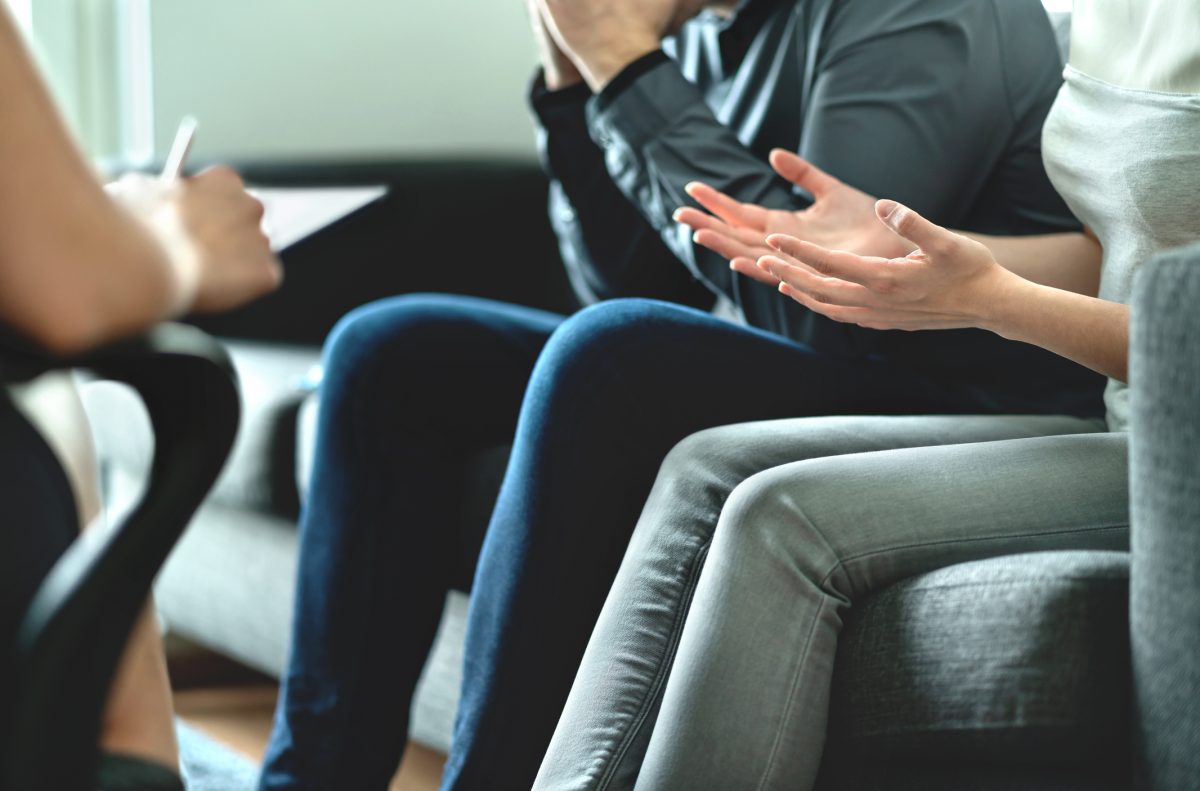 Two people on a couch talk to a third person in a chair opposite.