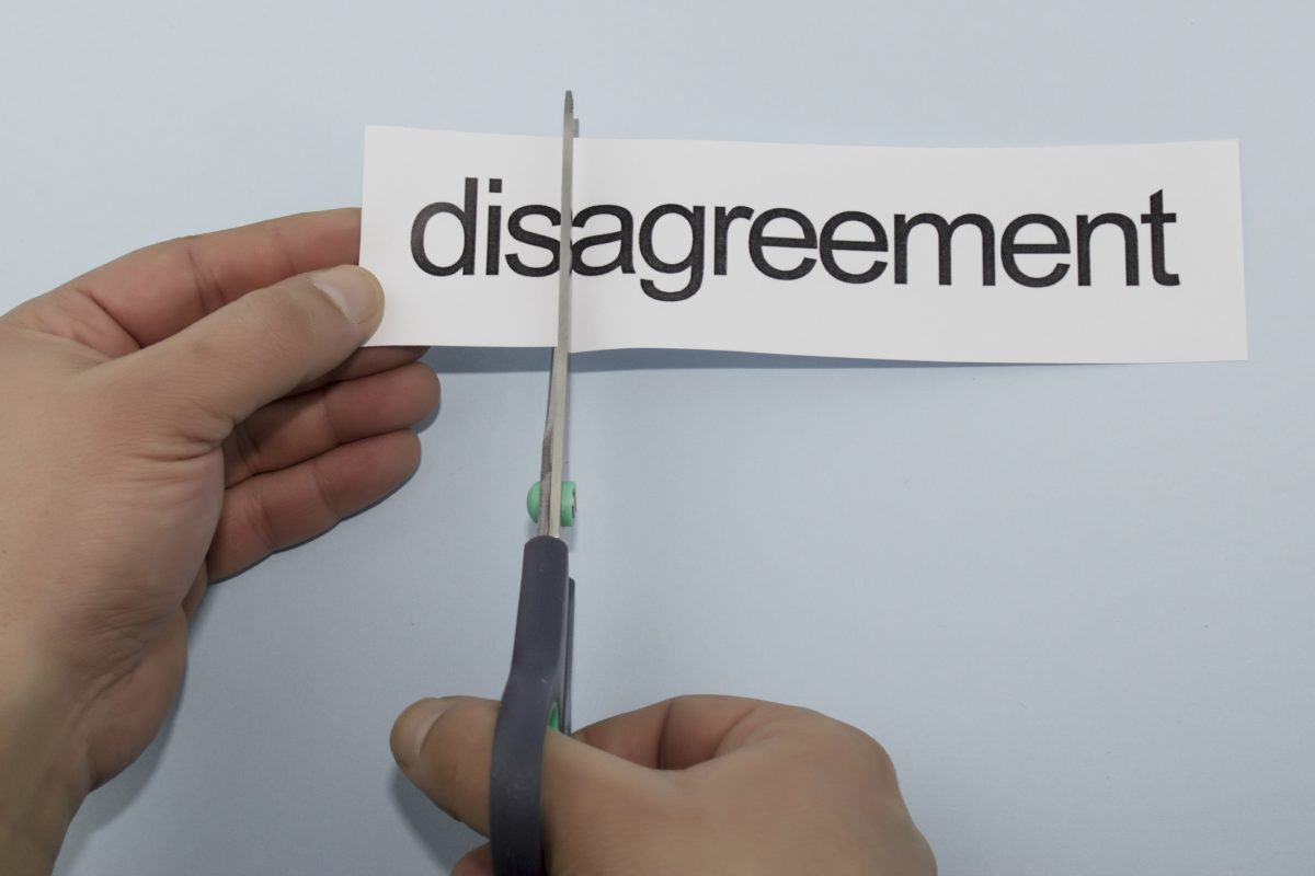 Scissors cut the letters `dis' away from `agreement' on a piece of paper.