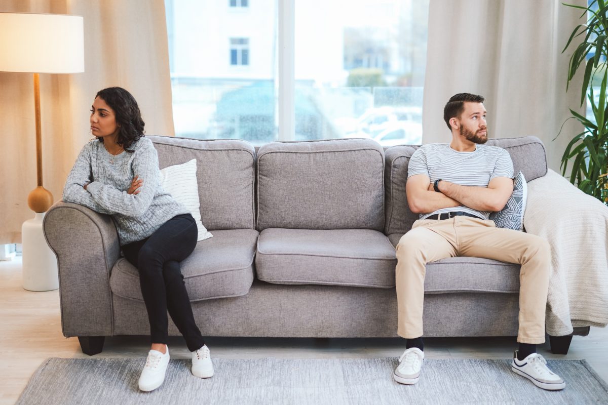 A man and woman on a couch look away from each other.