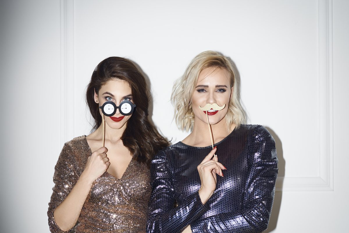 two women posing for a photobooth holding up props