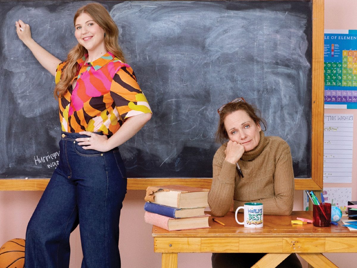 Girls standing and writing on the chalkboard and woman sitting next to her