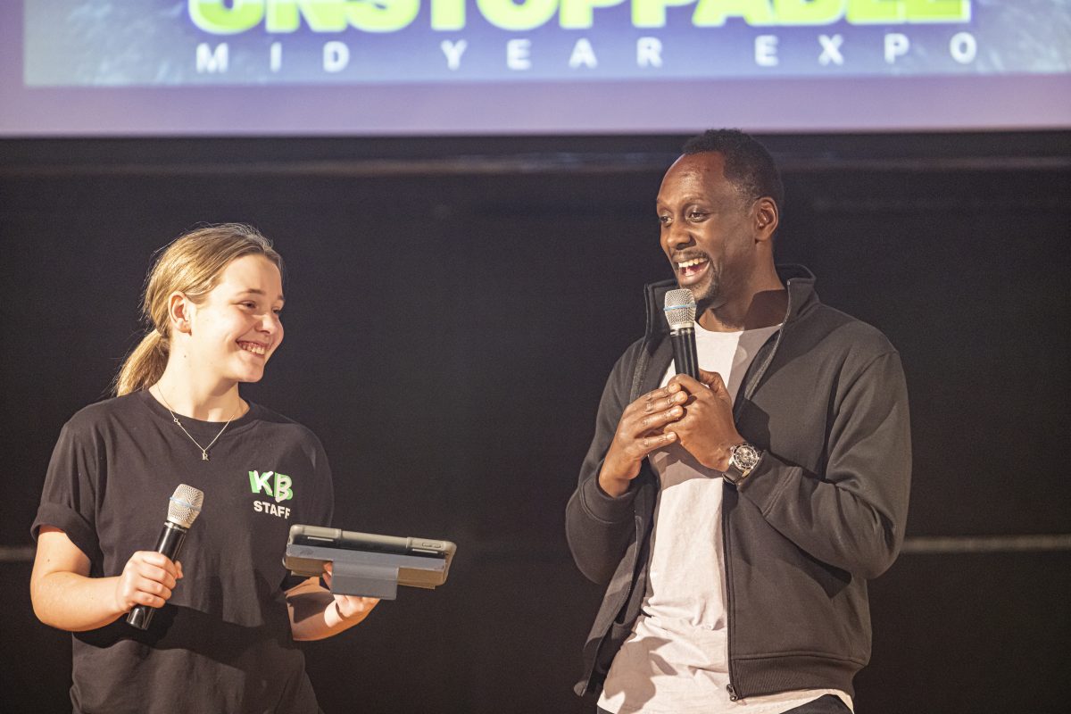 Francis Owusu giving a speech on stage next to a dance student