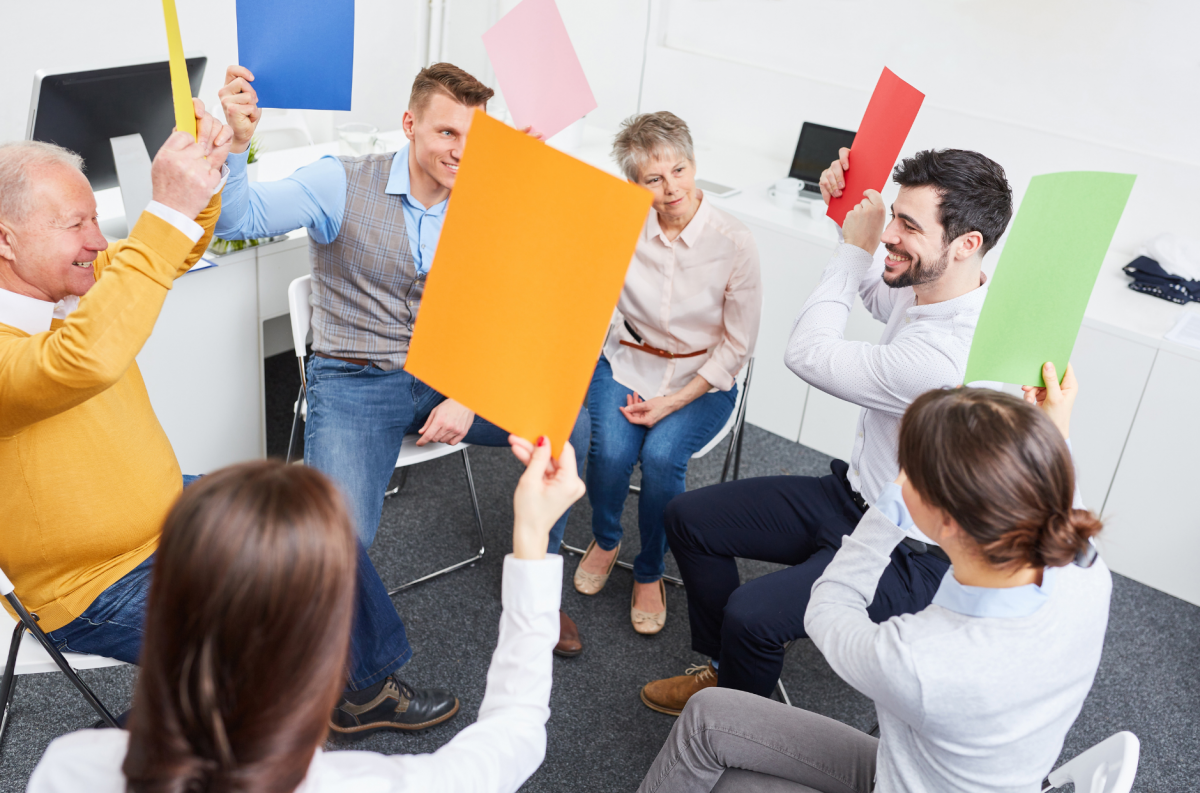 Six seated people hold up large coloured cards