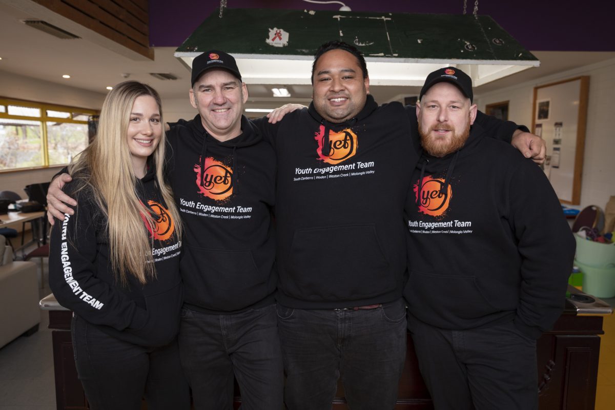 Four people stand arm in arm wearing Youth Engagement Team outfits.