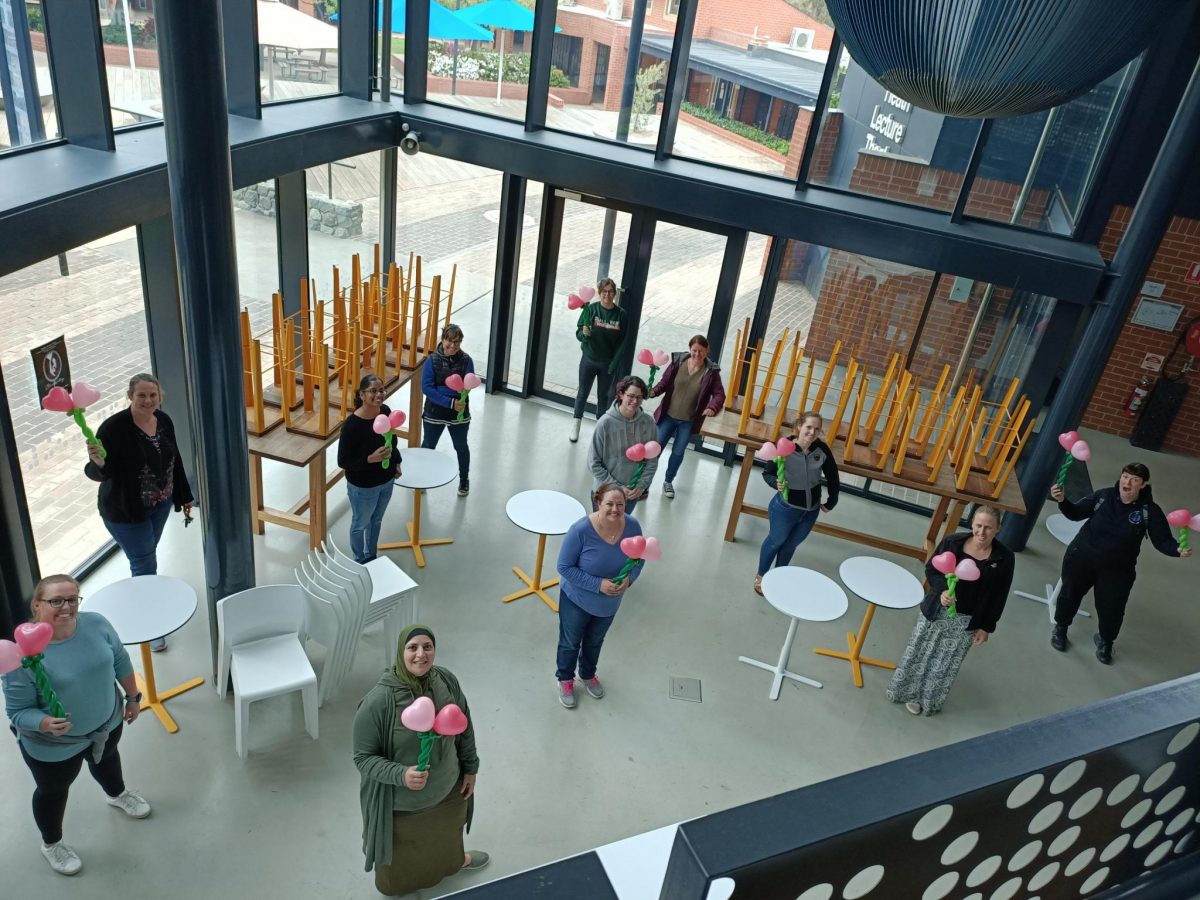 Twelve Mega Mums hold up twin pink heart-shaped balloons