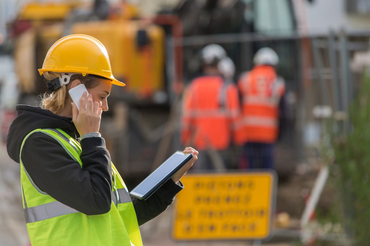 Woman wearing a hard hat and high vis vest on the phone at a construction site