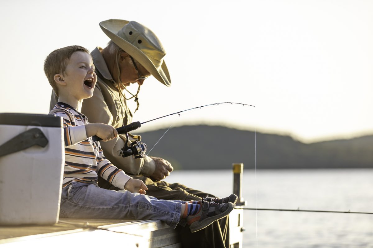 A grandfather and grandson sitting on the dock and laughing as they fish