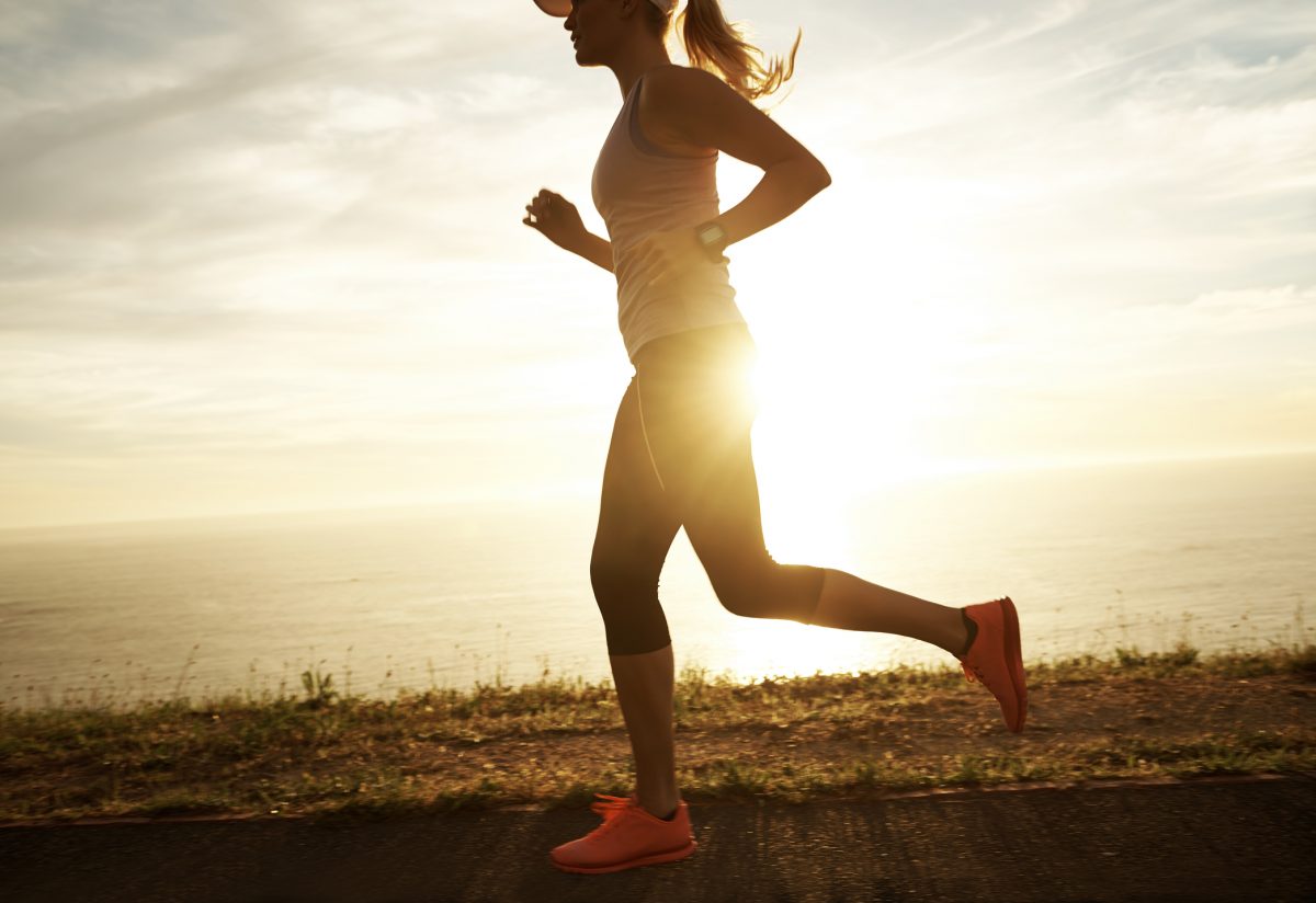 A young woman running along a coastal road with the sun setting behind her