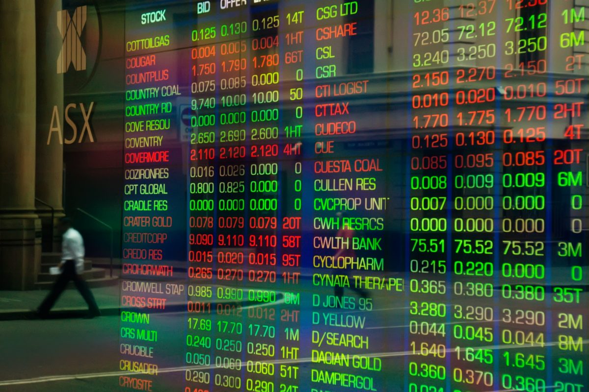 An office worker crossing a road is reflected in the glass display of a trading screen at the Australian Stock Exchange on Bridge Street