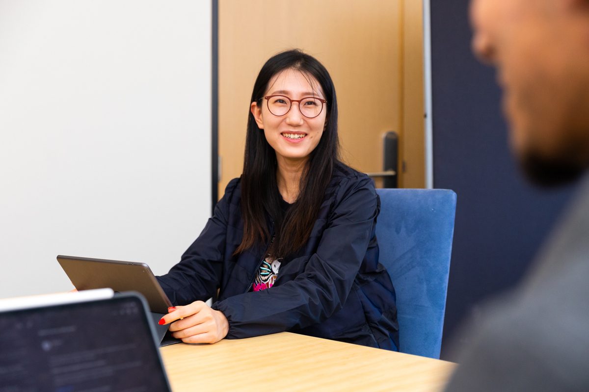 Female student in front of a tablet smiling at someone in the foreground