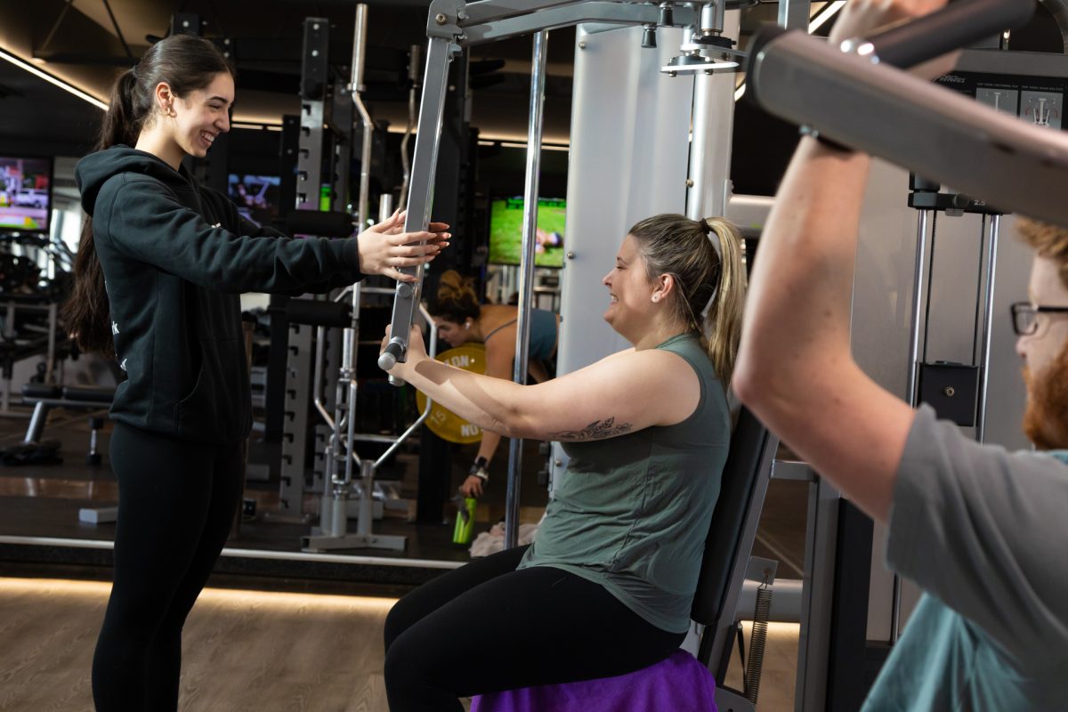 An Anytime Fitness personal trainer guides a client through a workout on gym equipment