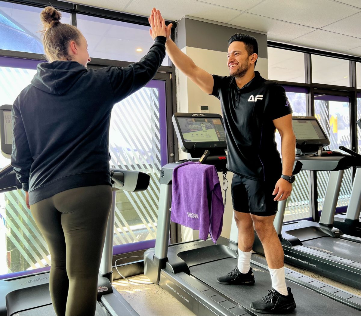 Man on treadmill hi-fiving his personal trainer at an Anytime Fitness gym. 
