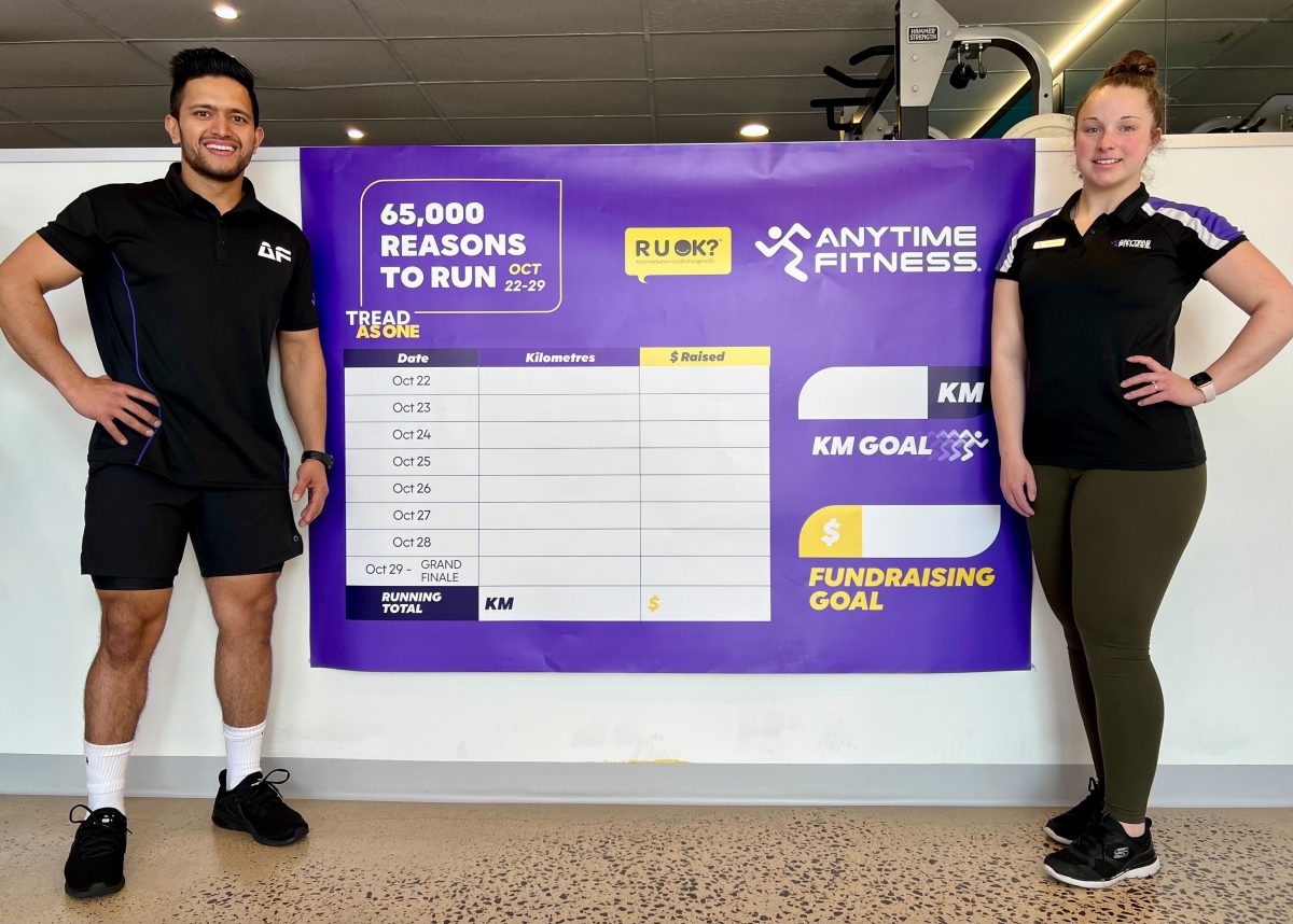 Personal trainers at an Anytime Fitness gym flanking a Tread As One fundraising leaderboard