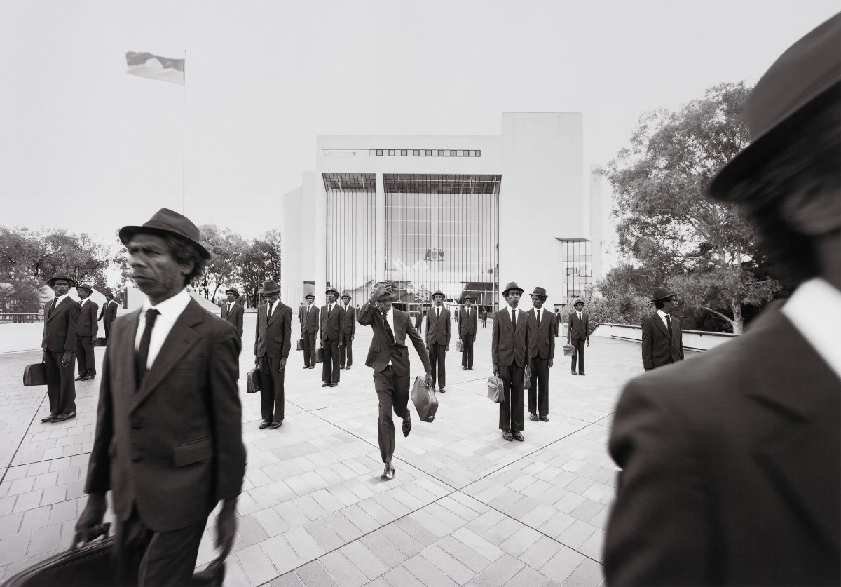 Black and white photo of a man in a suit and hat multiplied walking in front of a courthouse