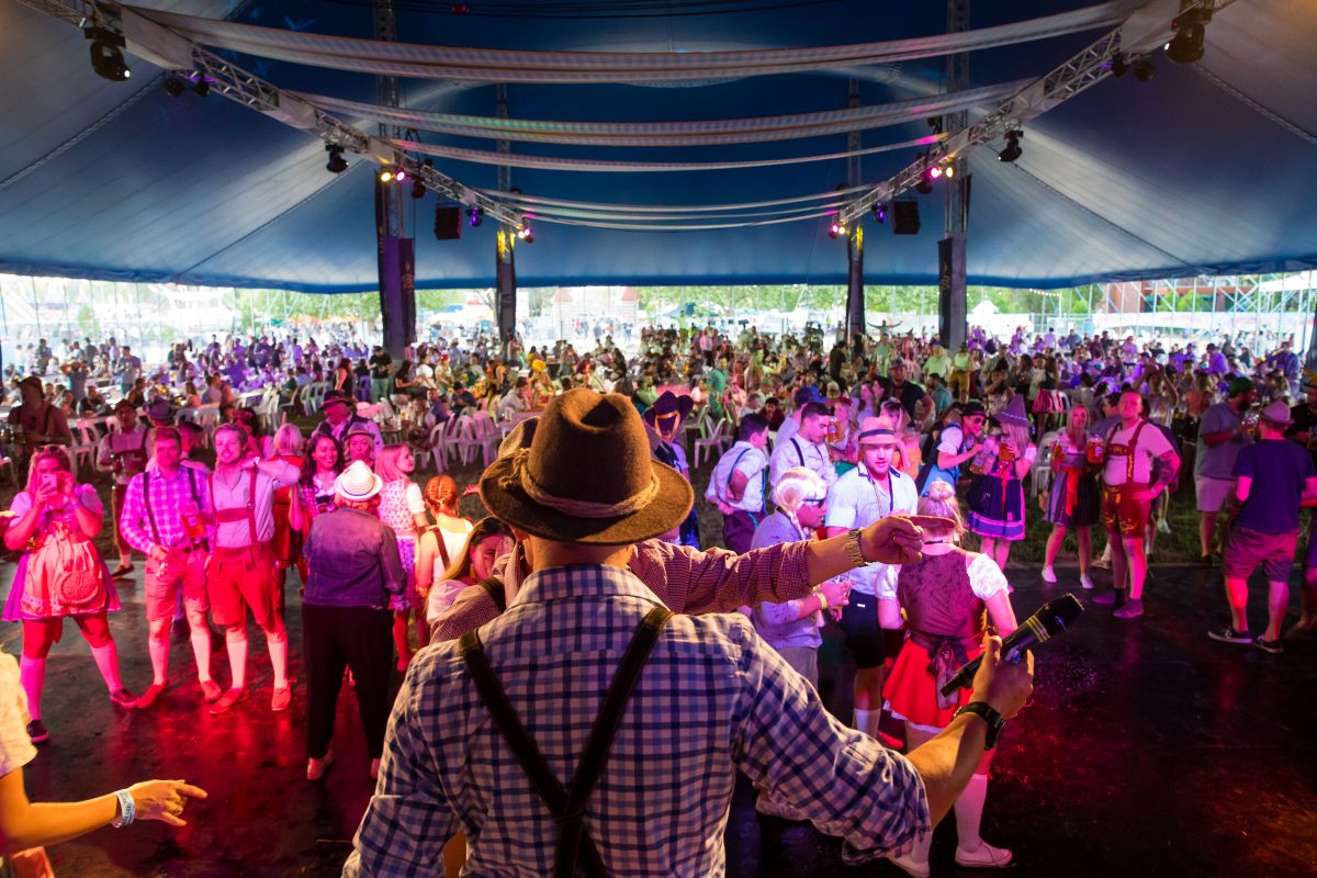 Back of man wearing a hat on stage in front of huge crowd dressed in traditional German garb