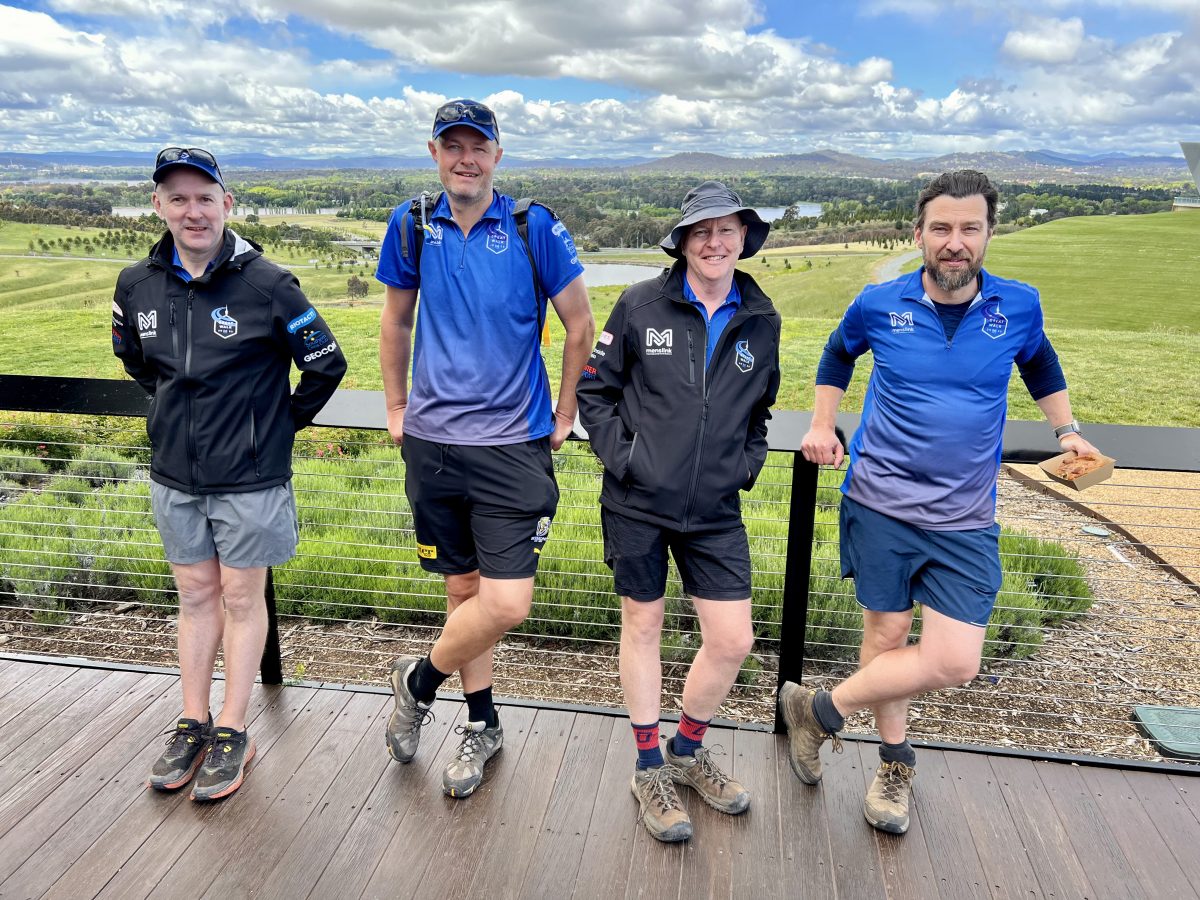 Four men leaning against fence