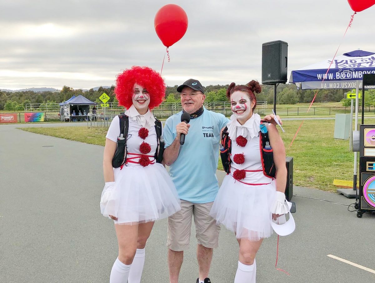 2022 Stromlo Running Festival volunteers Shannon Schuster and Amy Mckenzie dressed as clowns and flanking the event MC