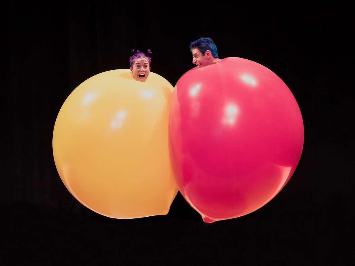 People in giant balloons against a black background