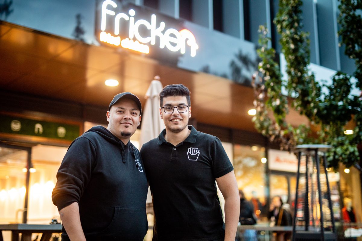 two brothers smile at camera in front of logo