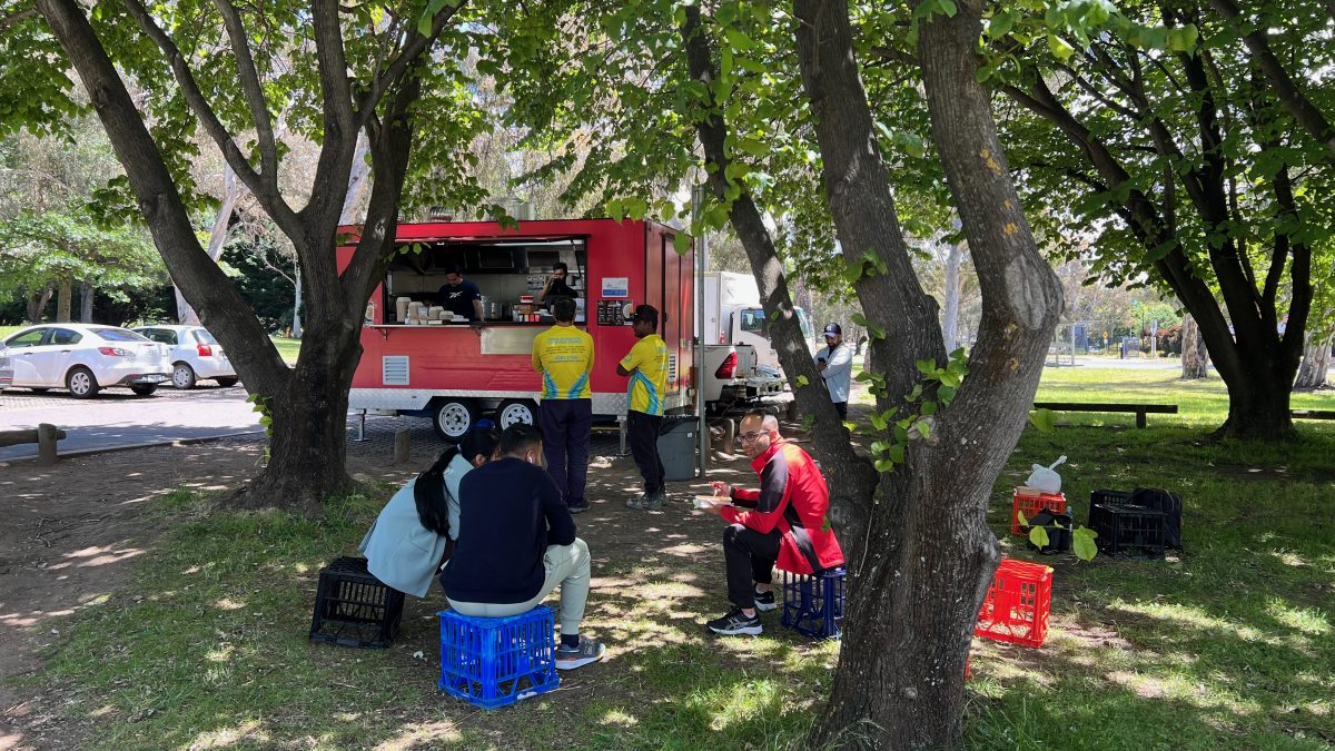 People sitting under trees on crates in front of red truck