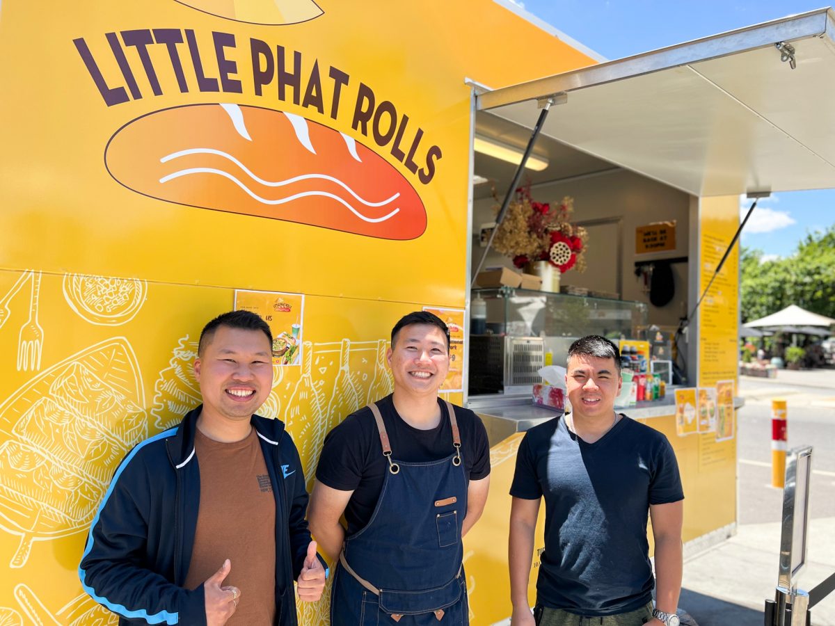 three men stand in front of yellow food truck