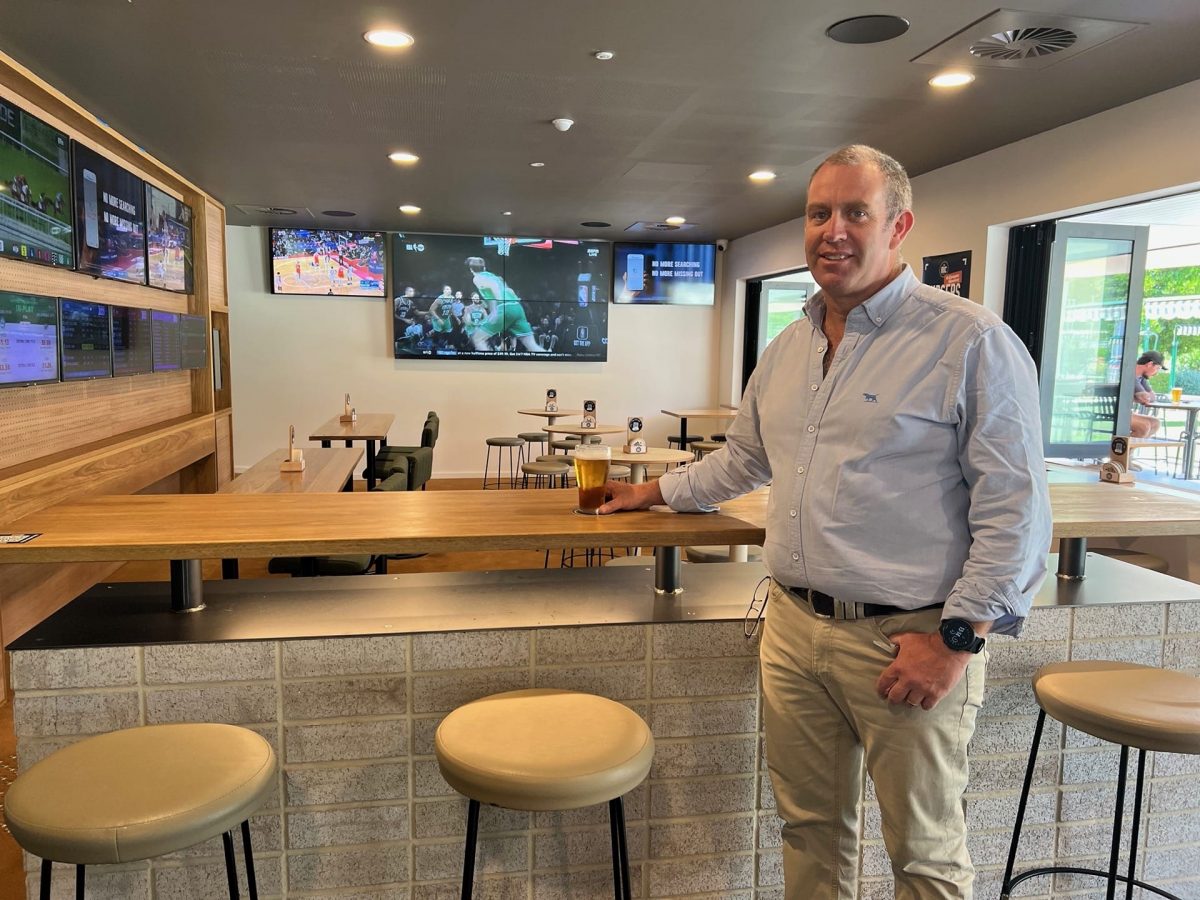 Ned Scanlon holds a beer in front of TVs showing sports